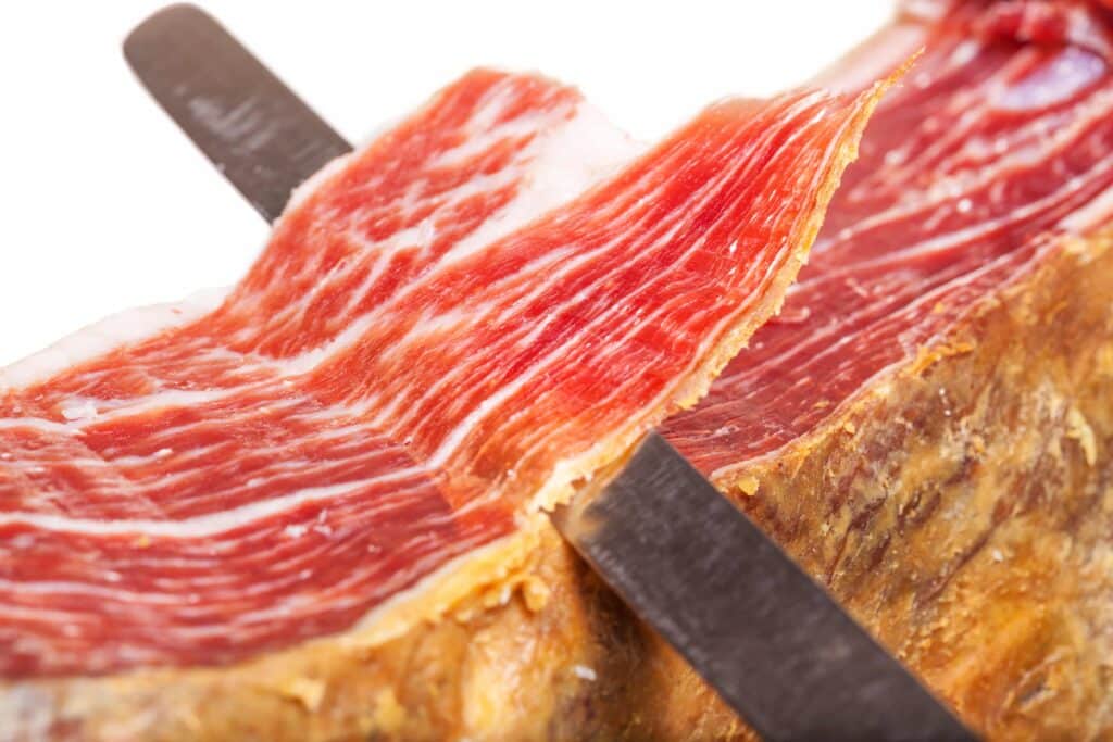 Foto em zoom de uma lâmina cortando pedaços de Jamón Ibérico.