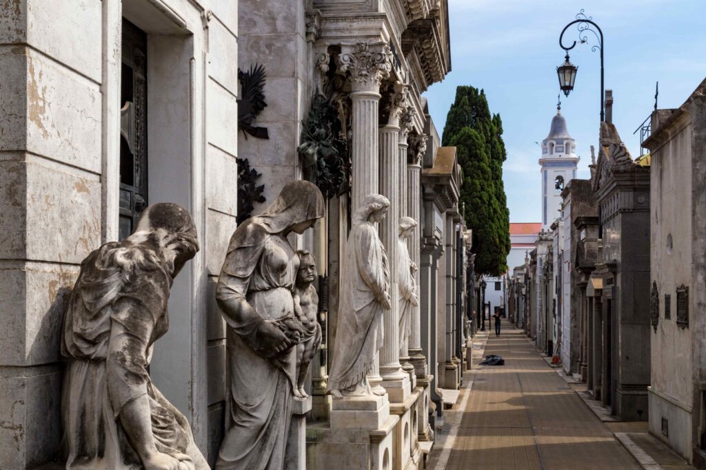 Foto de uma das alamedas do cemitério da Recoleta, em Buenos Aires, Argentina. Foco em esculturas em estilo romano.